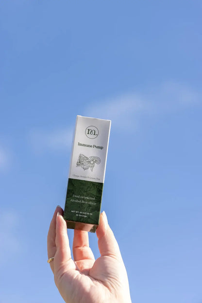 Hand holding a skincare product against a clear blue sky