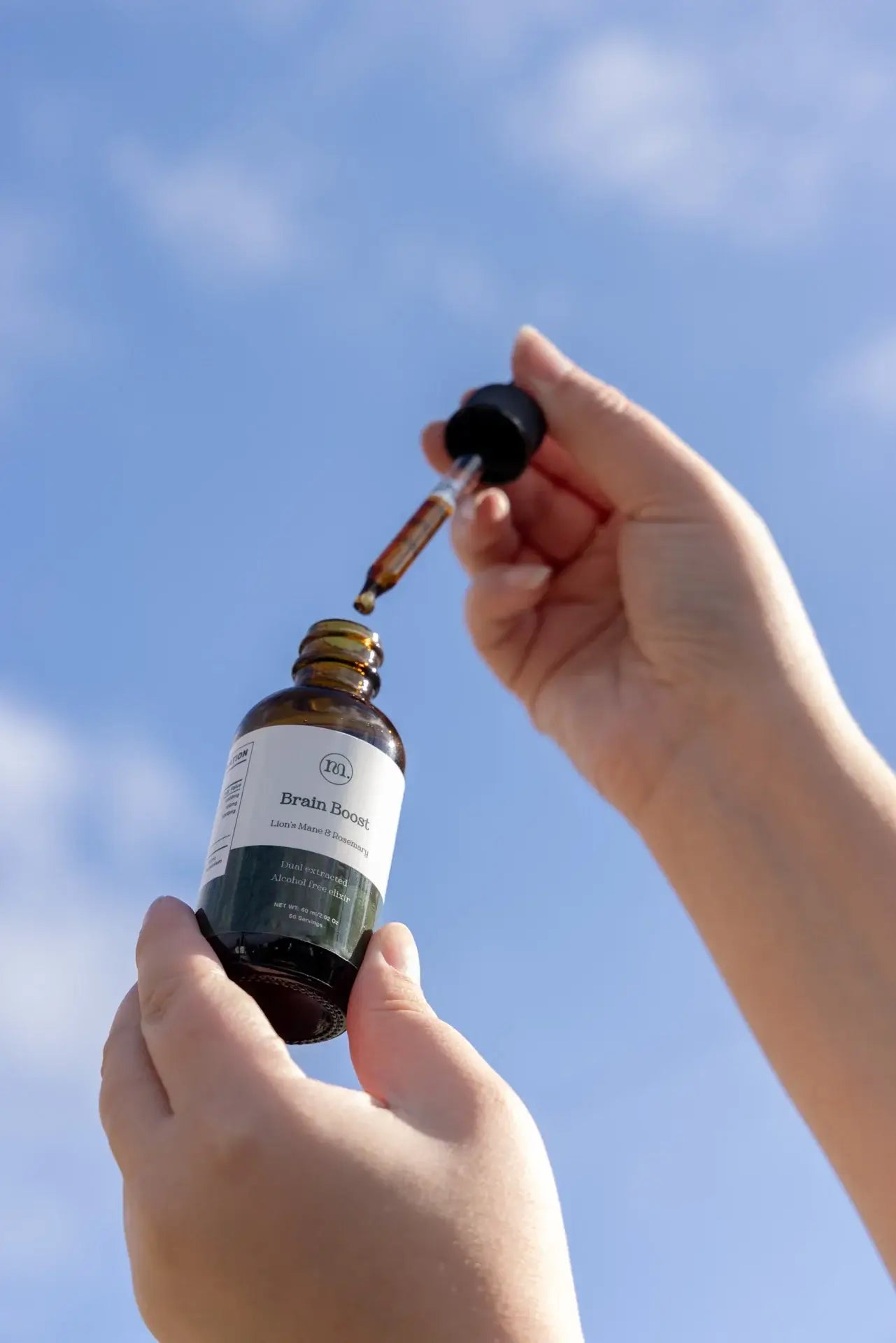 Hand holding a dropper over a bottle against a blue sky