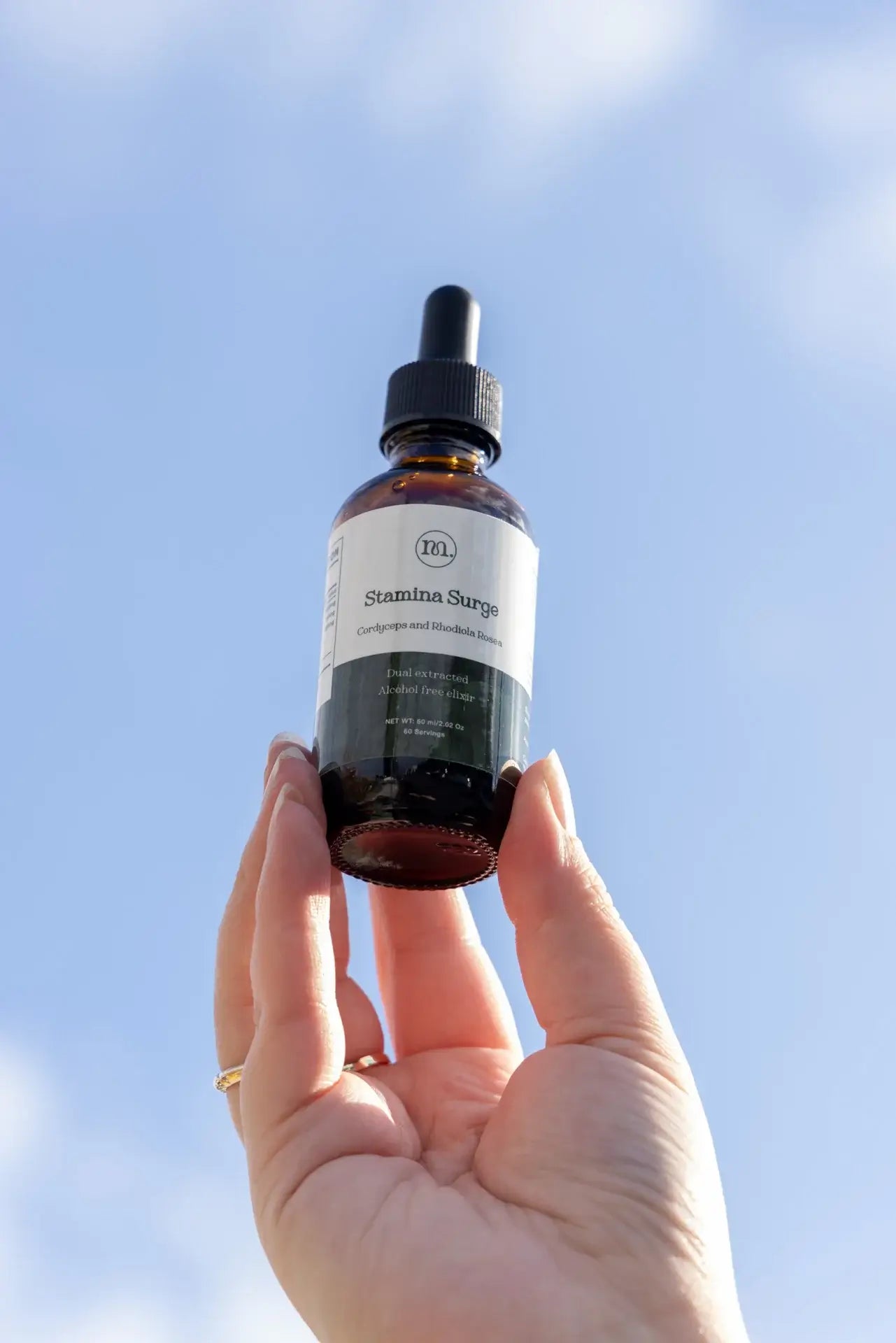 Hand holding a bottle of skincare serum against a blue sky