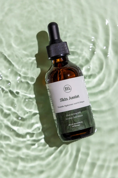 Brown glass bottle with dropper labeled 'Skin Assistan' on a light green water background