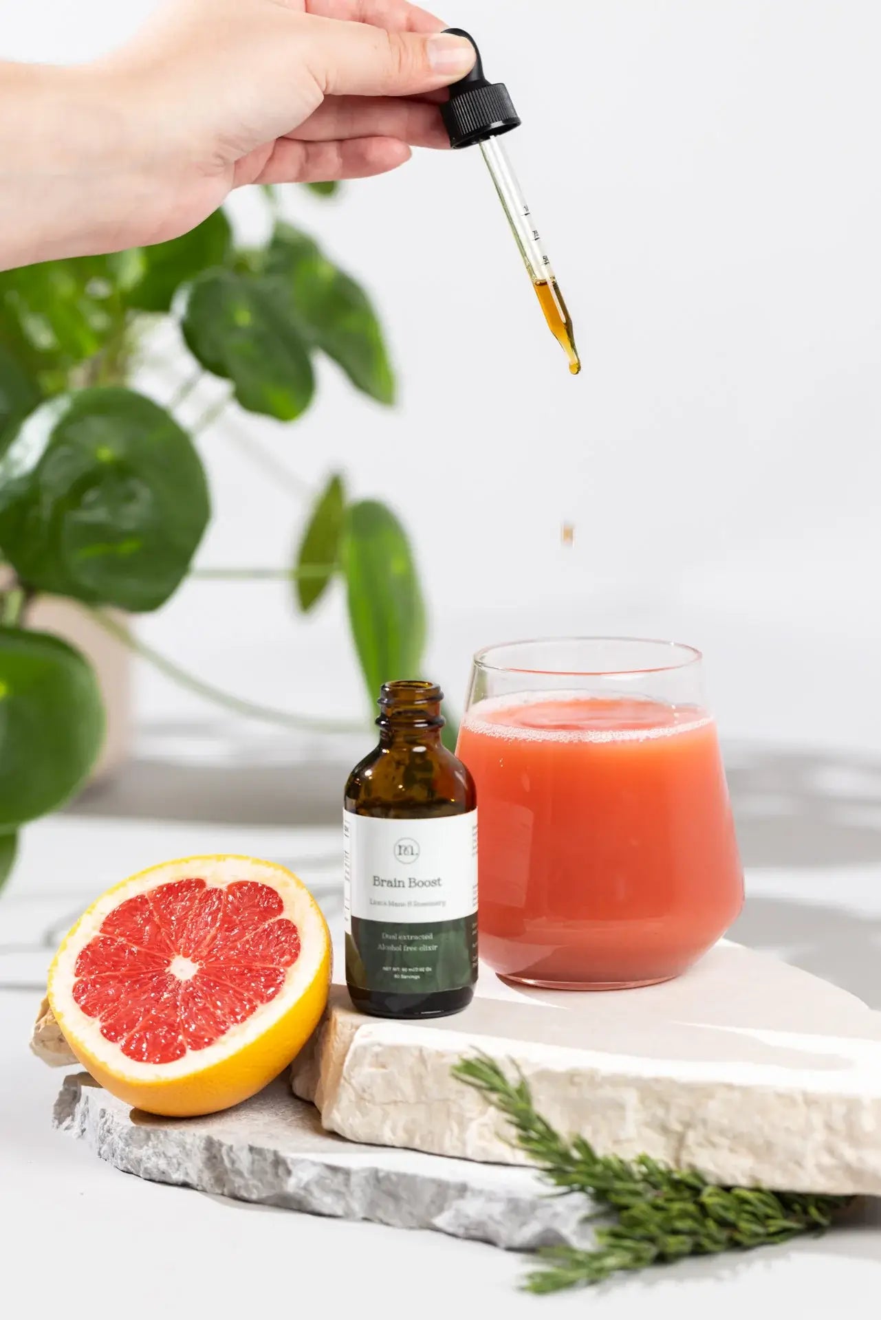 Hand holding a dropper over a glass of red juice with a bottle labeled 'Pineapple' on a white surface.