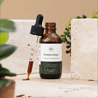 Bottle of 'Stamina Surge' with dropper on a stone surface with plants in the background